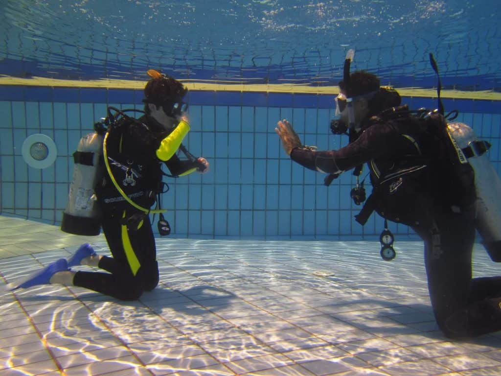 do you have to know how to swim to scuba dive - diving instructor is showing hand signals to the student in the pool