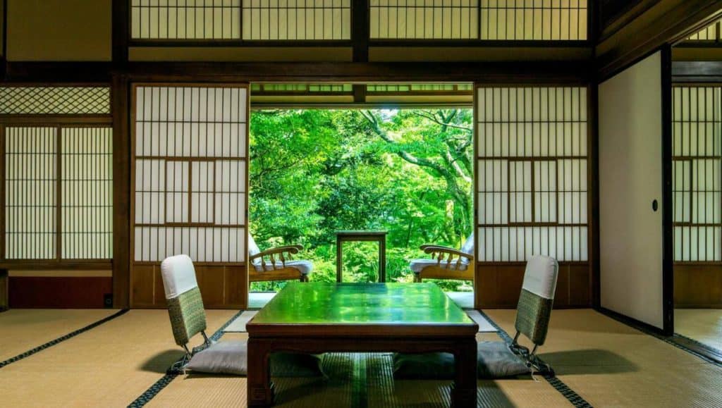 ryokan with private onsen in hakone - a traditional seating area with tatami flooring in one of the rooms at Gora Kansuiro surrounded by lush greenery