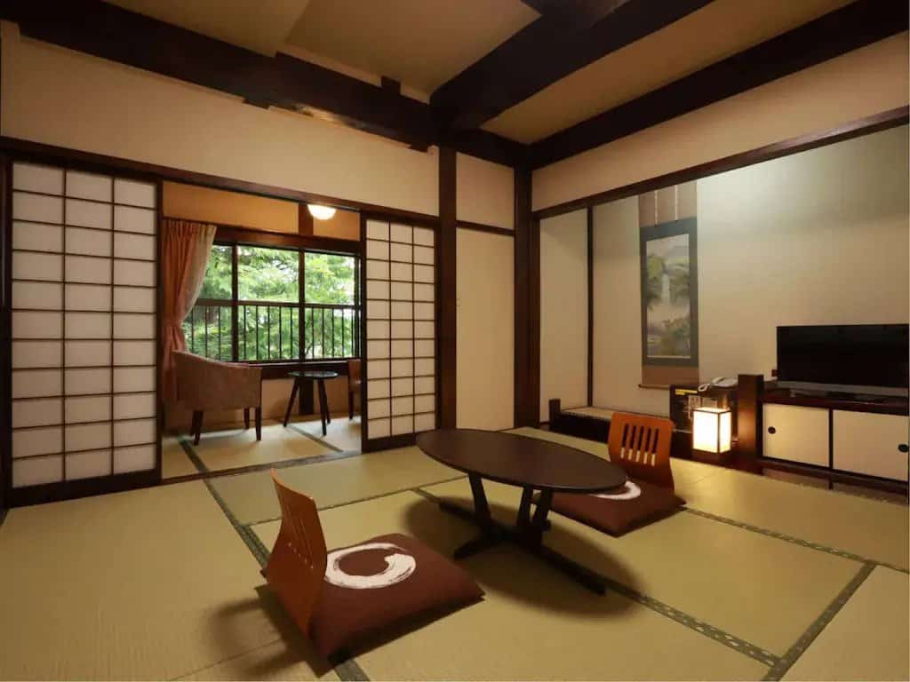 takayama onsen ryokan -  a tatami-floored room with 2 seats and tables and a view of the trees in Ryokan Murayama