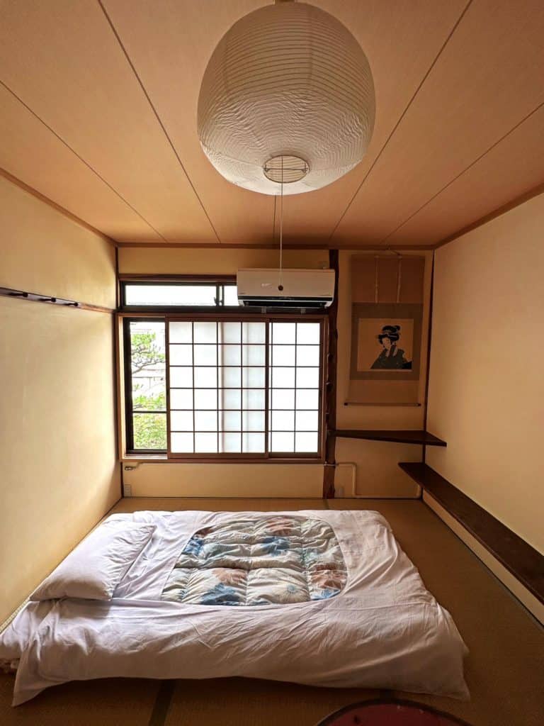 best ryokan in osaka - a tatami bed with sliding shoji window and a Japanese drawing in a ryokan room