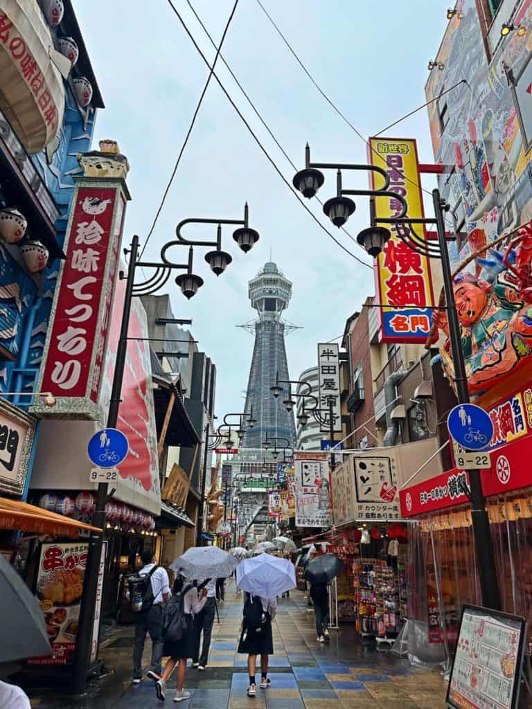 is osaka safe for solo travelers - locals walking while holding the umbrella at Shinsekai with Tsutenkaku Tower as the backdrop 