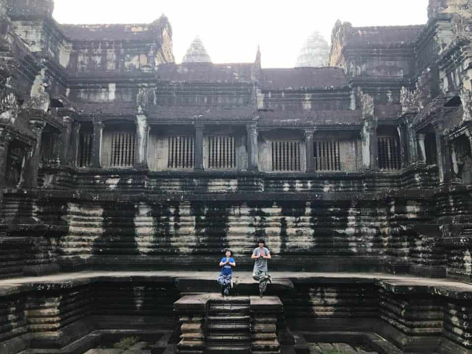 Two people standing on one leg and bend the other at one of the temples in Angkor Wat, Cambodia