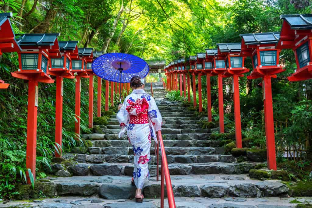 Kifune Shrine in Kyoto - a lady dressed in kimono is holding a traditional umbrella while walking up the stairs in Kifune Shrine