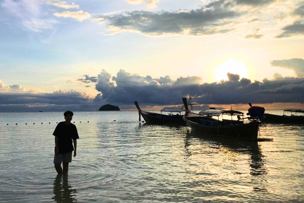 Sam Lee Travel - me stood in the sea water with the boats as the backdrop during sunrise at Koh Lipe, Thailand