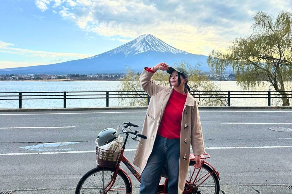 where to stay at fuji kawaguchiko - me holding my cap standing in front of the rental bike with Mount Fuji and Lake Kawaguchiko as the backdrop