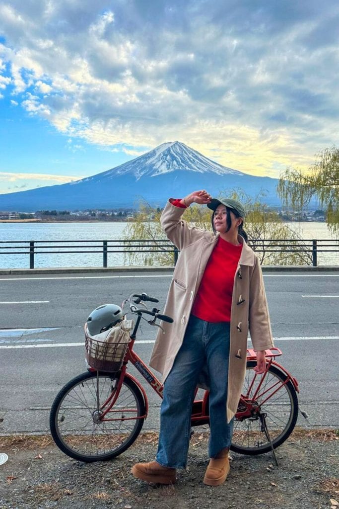 cycling around mount fuji lake kawaguchiko route - me holding my cap while standing in front of the rental bike with Mount Fuji and Lake Kawaguchiko as the backdrop