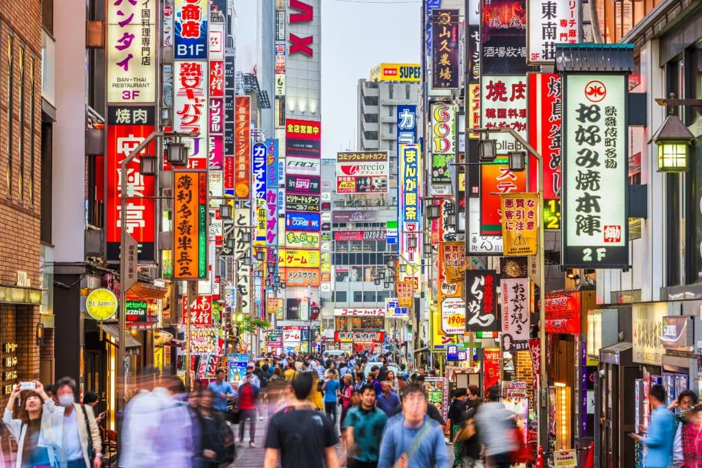 how to plan a trip to japan as first-time visitor - a shot of Shibuya where people walking on the street lined with multiple neon dashboards on both sides